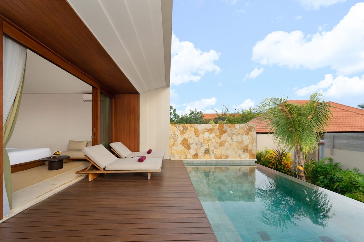 Uma área moderna com piscina ao ar livre, deck de madeira, espreguiçadeiras e uma parede de pedra.
