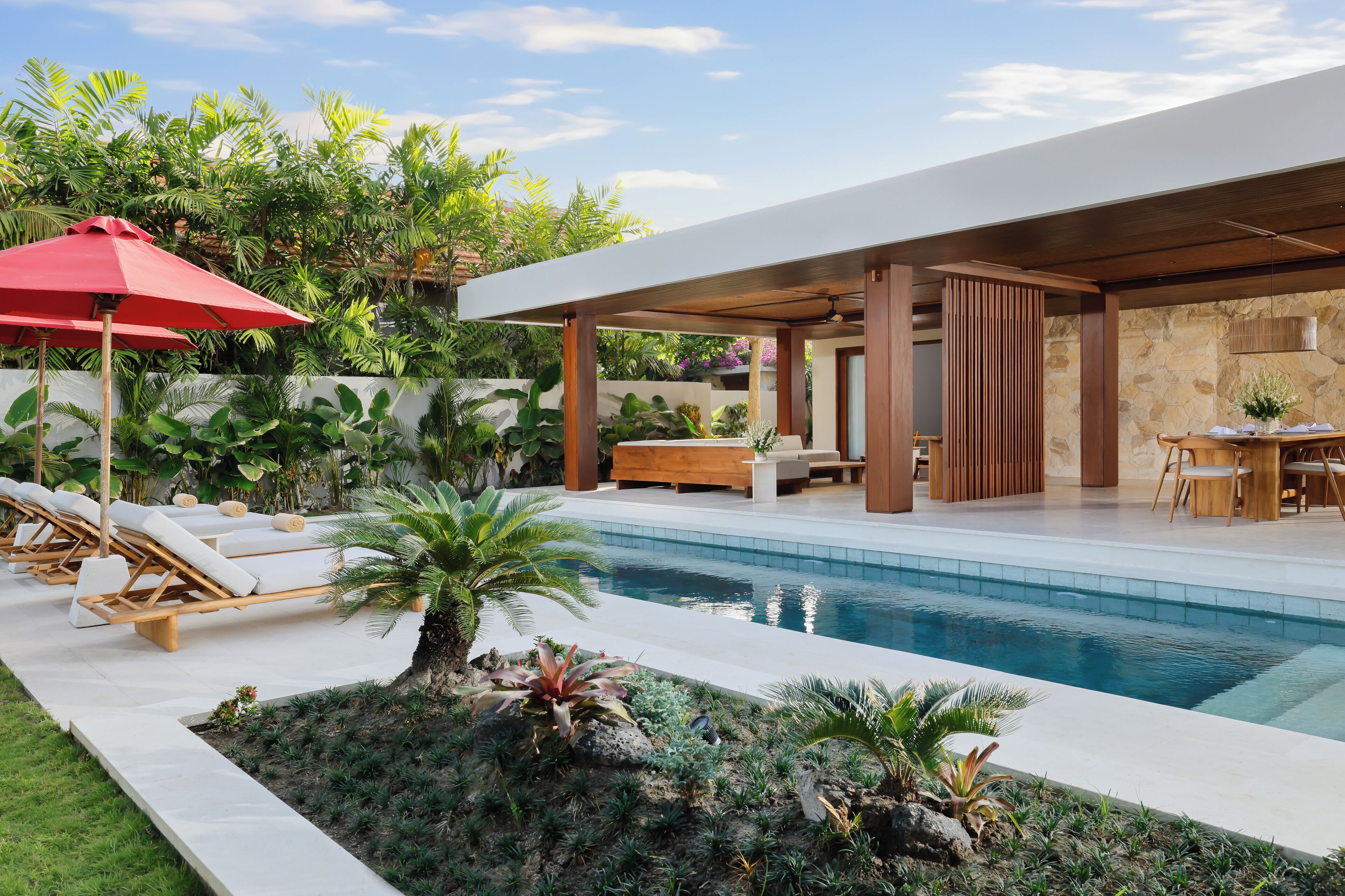 A modern outdoor pool area with lounge chairs, a red umbrella, and lush greenery.