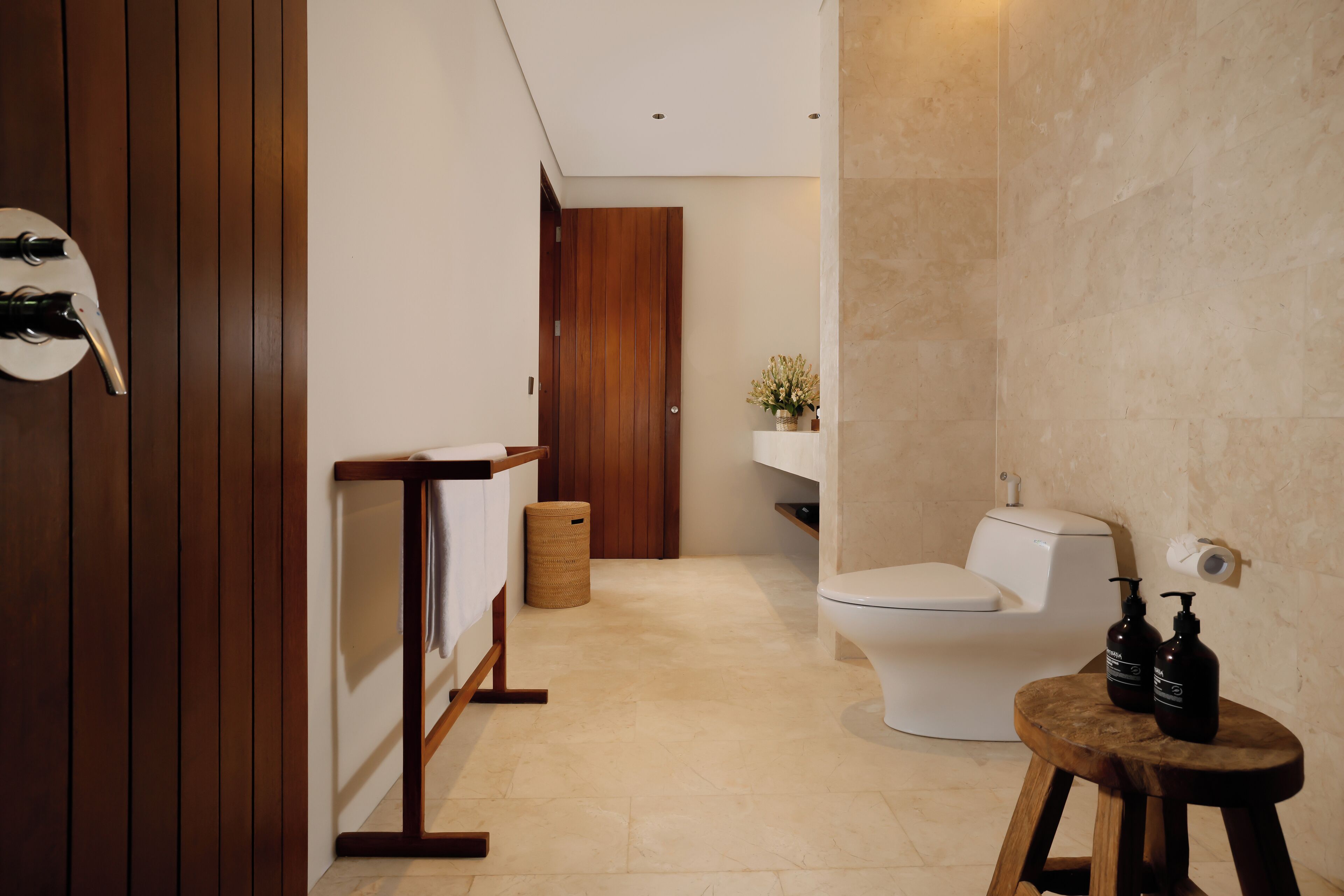 A modern bathroom with a wooden vanity, a toilet, and a small stool with toiletries.