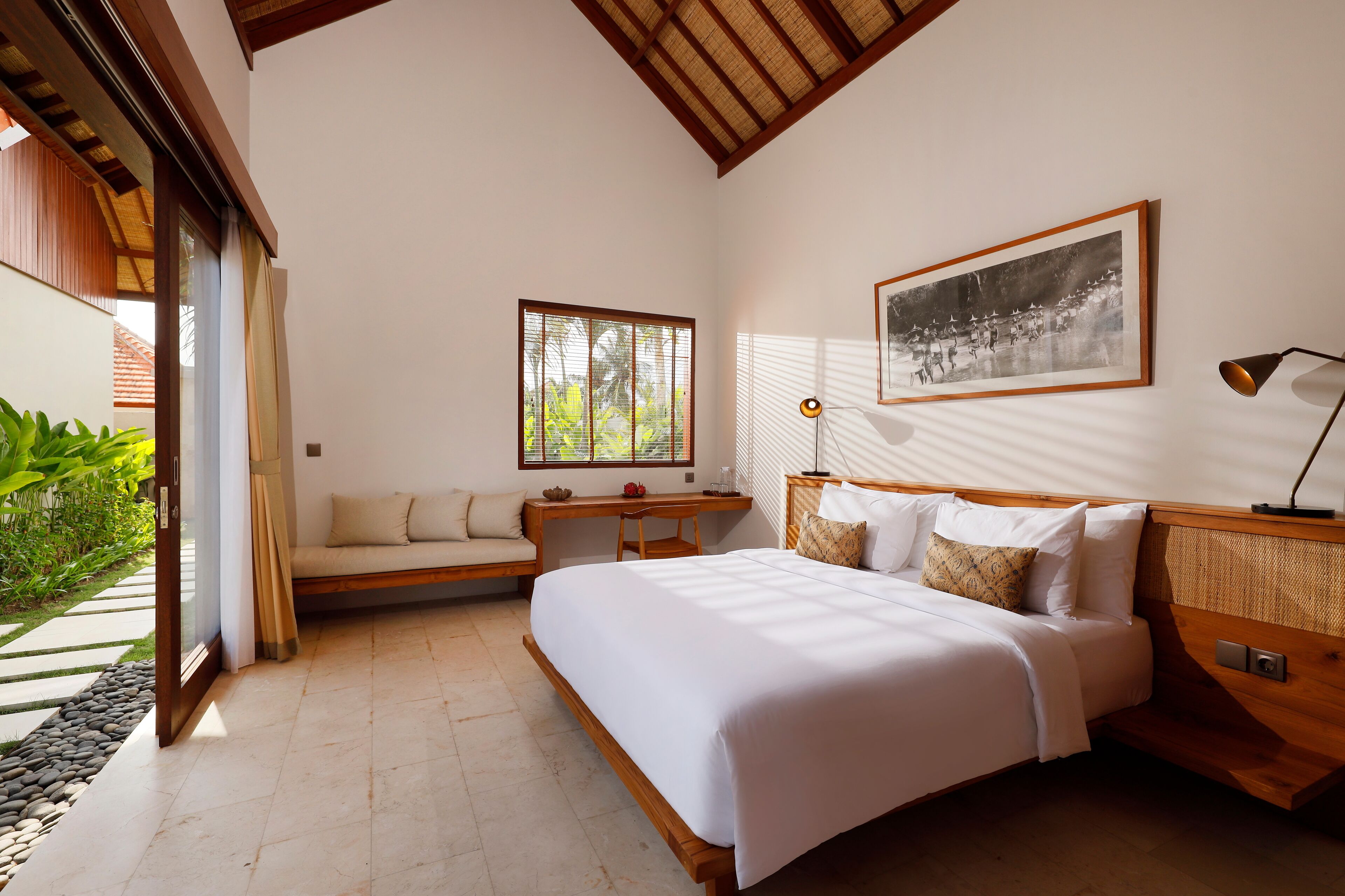 A bedroom with a large bed, a desk, and a window overlooking greenery.