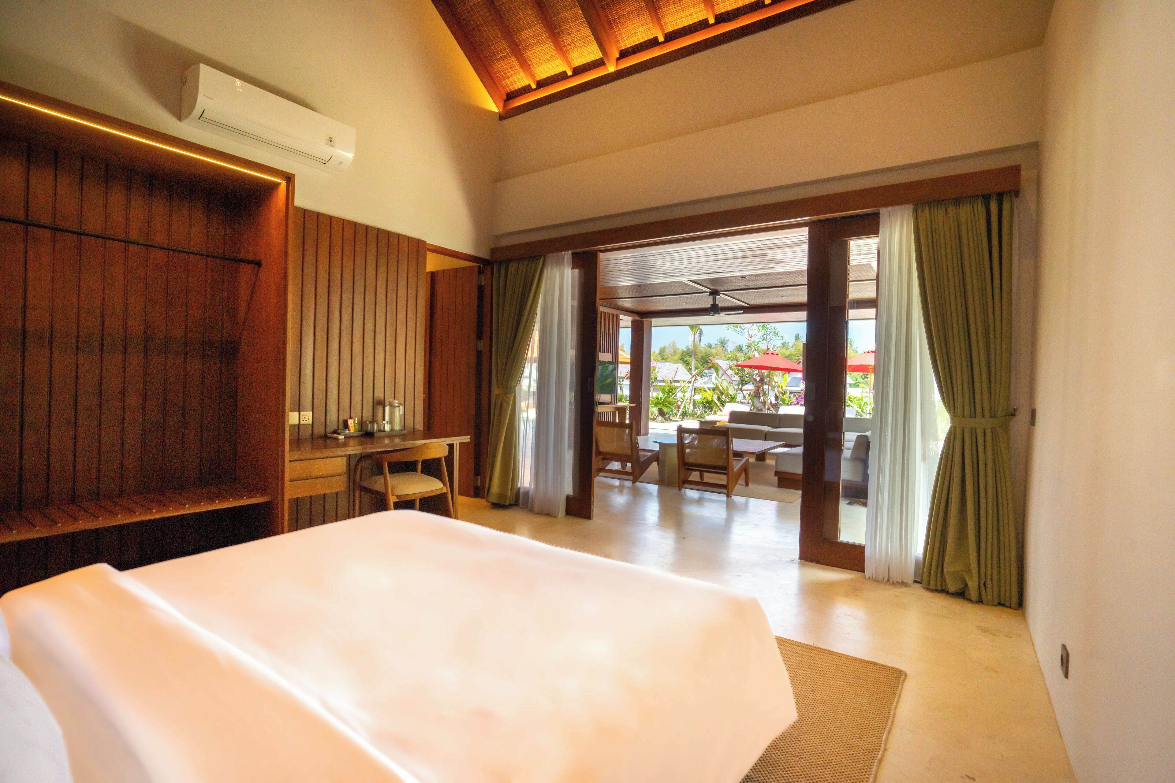 A hotel room with a large bed, wooden paneling, a desk, and a view of an outdoor patio with furniture.