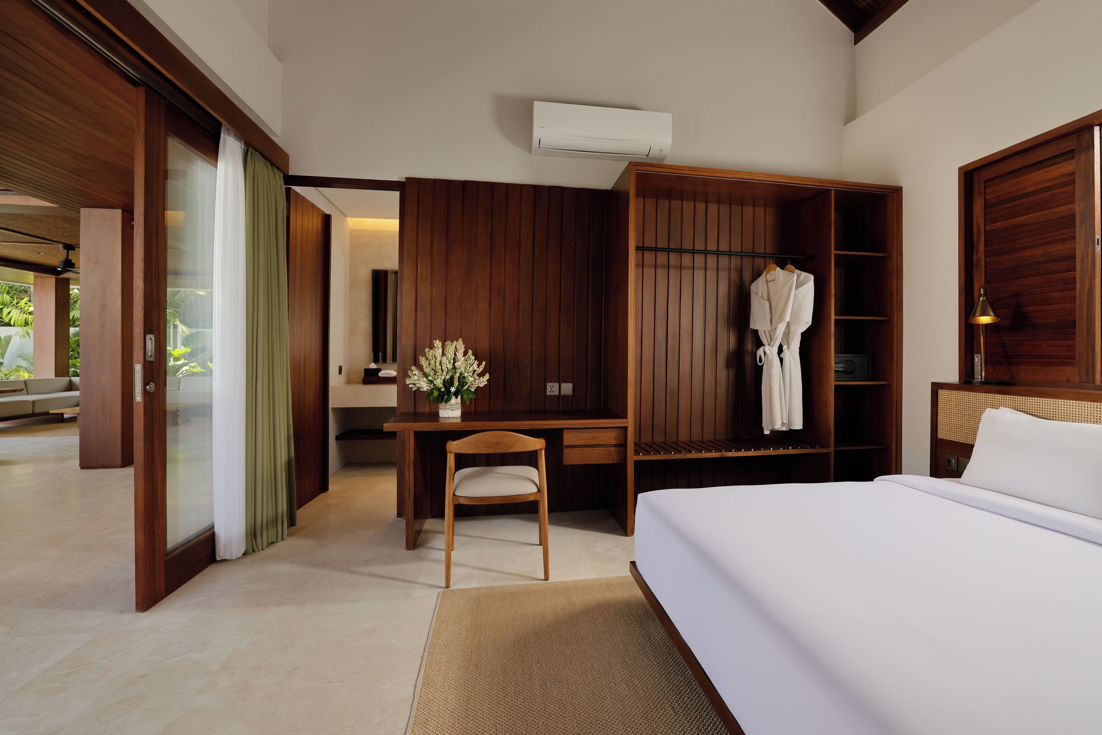 Una habitación de hotel moderna con una cama grande, un escritorio de madera, una silla, un armario y una pequeña mesa con un florero.