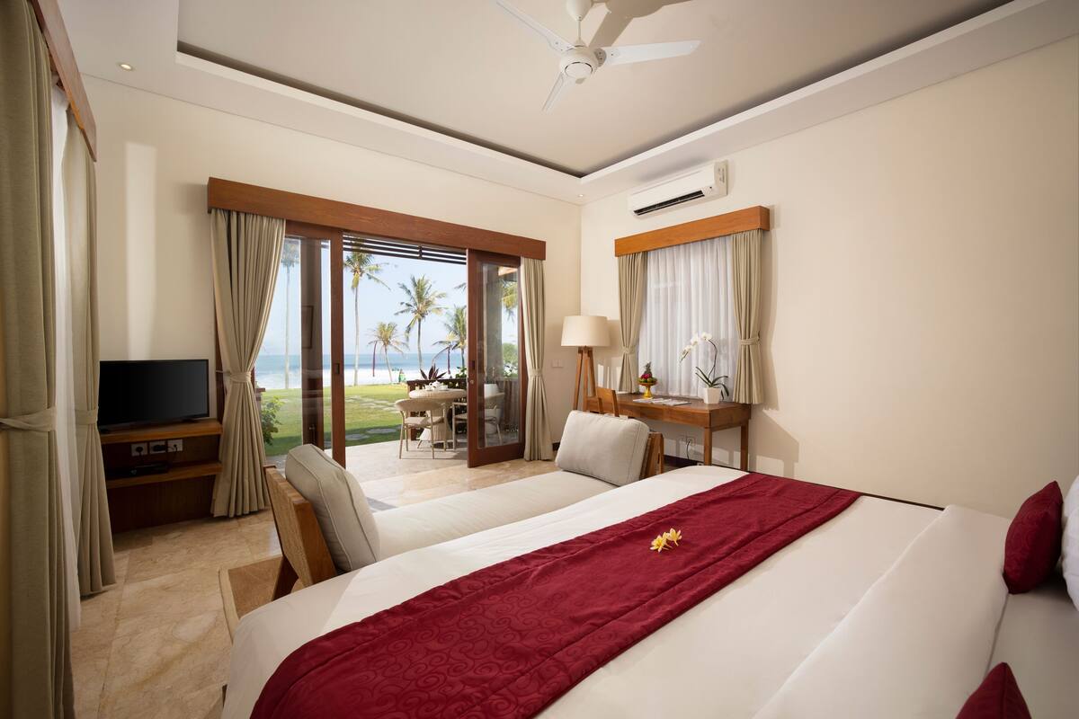 Quarto de hotel com cama, escrivaninha, televisão e vista para o oceano.