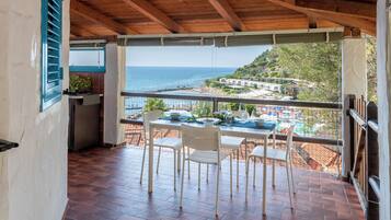 A balcony with a table and chairs, overlooking a beach and a hillside.
