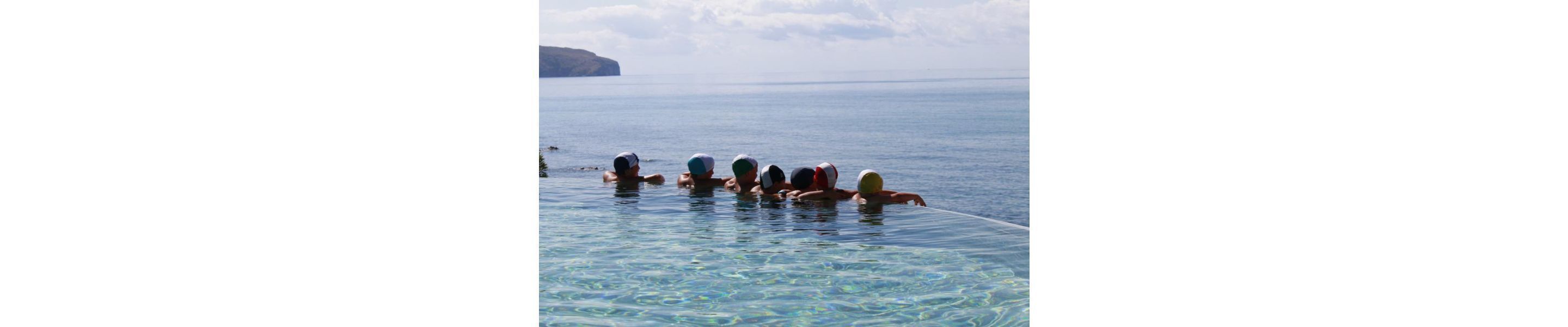 A group of people in a clear pool with a view of the sea and a distant landform.