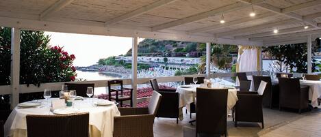 Un espace extérieur aménagé pour les repas, avec des tables et des chaises, offrant une vue panoramique sur la côte.