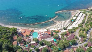 Vue aérienne d’une station balnéaire avec une piscine, une plage et plusieurs bâtiments aux toits rouges.