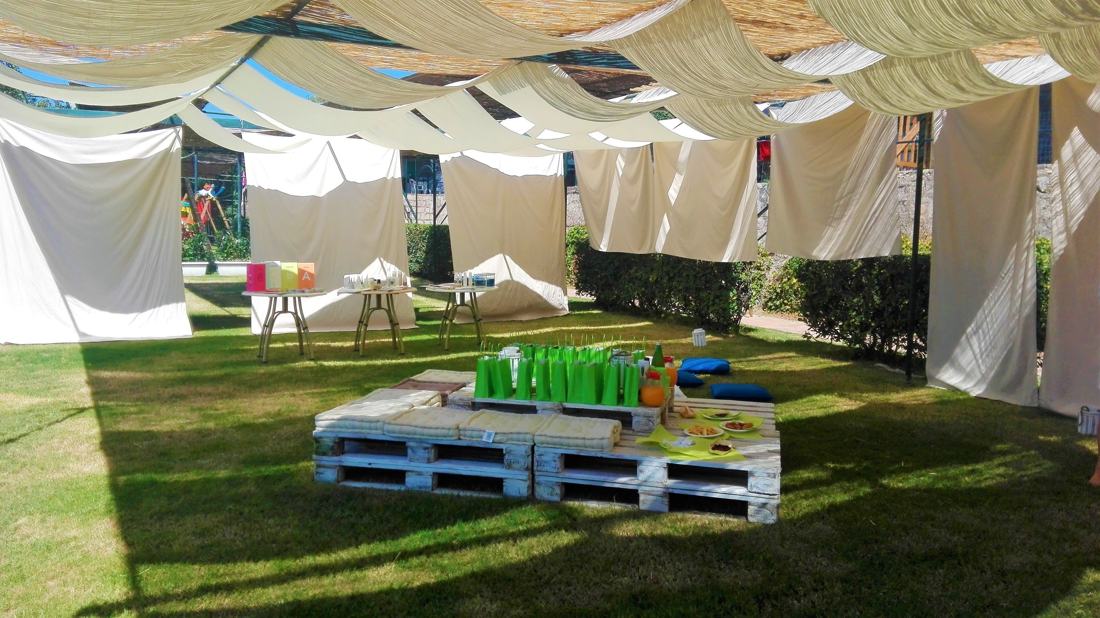 A tented outdoor area with tables and chairs, a table with green bags and food, and a grassy lawn.