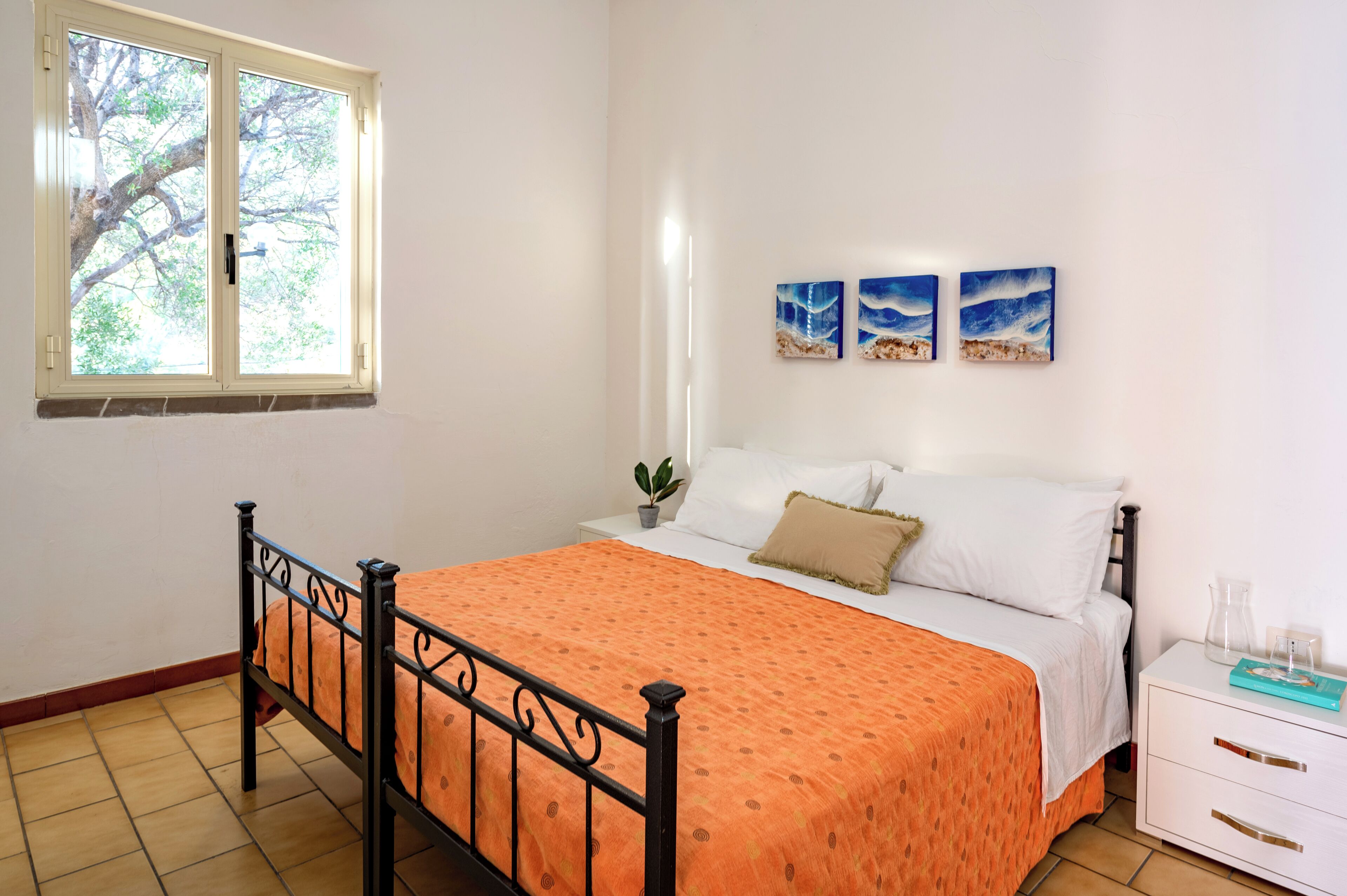 Een slaapkamer met een bed, nachtkastje, raam en wanddecoratie.