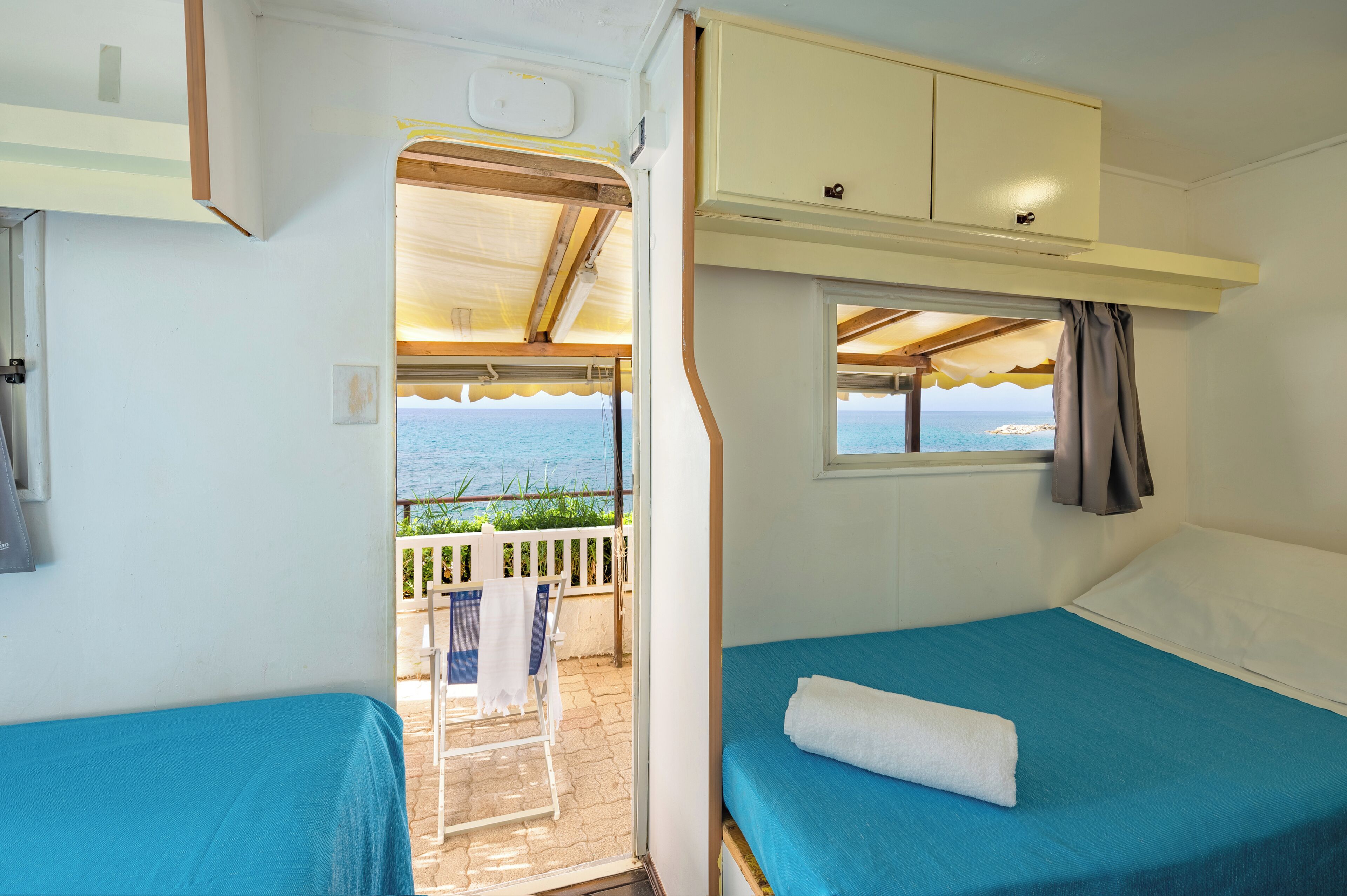 Ein kleines Zimmer mit zwei Betten, einem kleinen Fenster mit Vorhängen und Meerblick.
