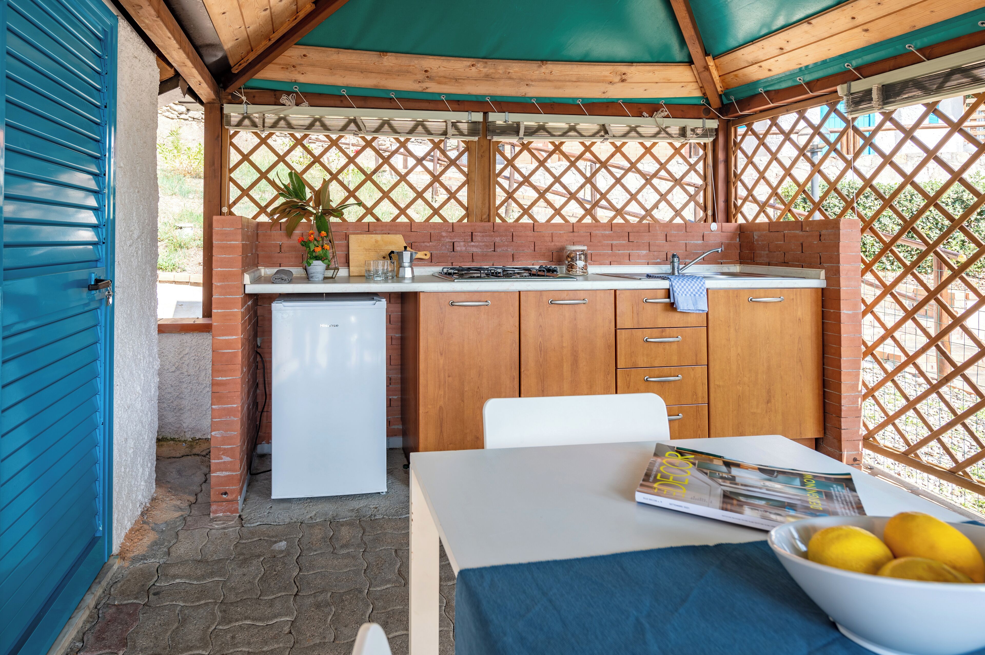 Una cocina al aire libre techada con un respuesto de ladrillo, un refrigerador blanco y una mesa con un bol de limones.