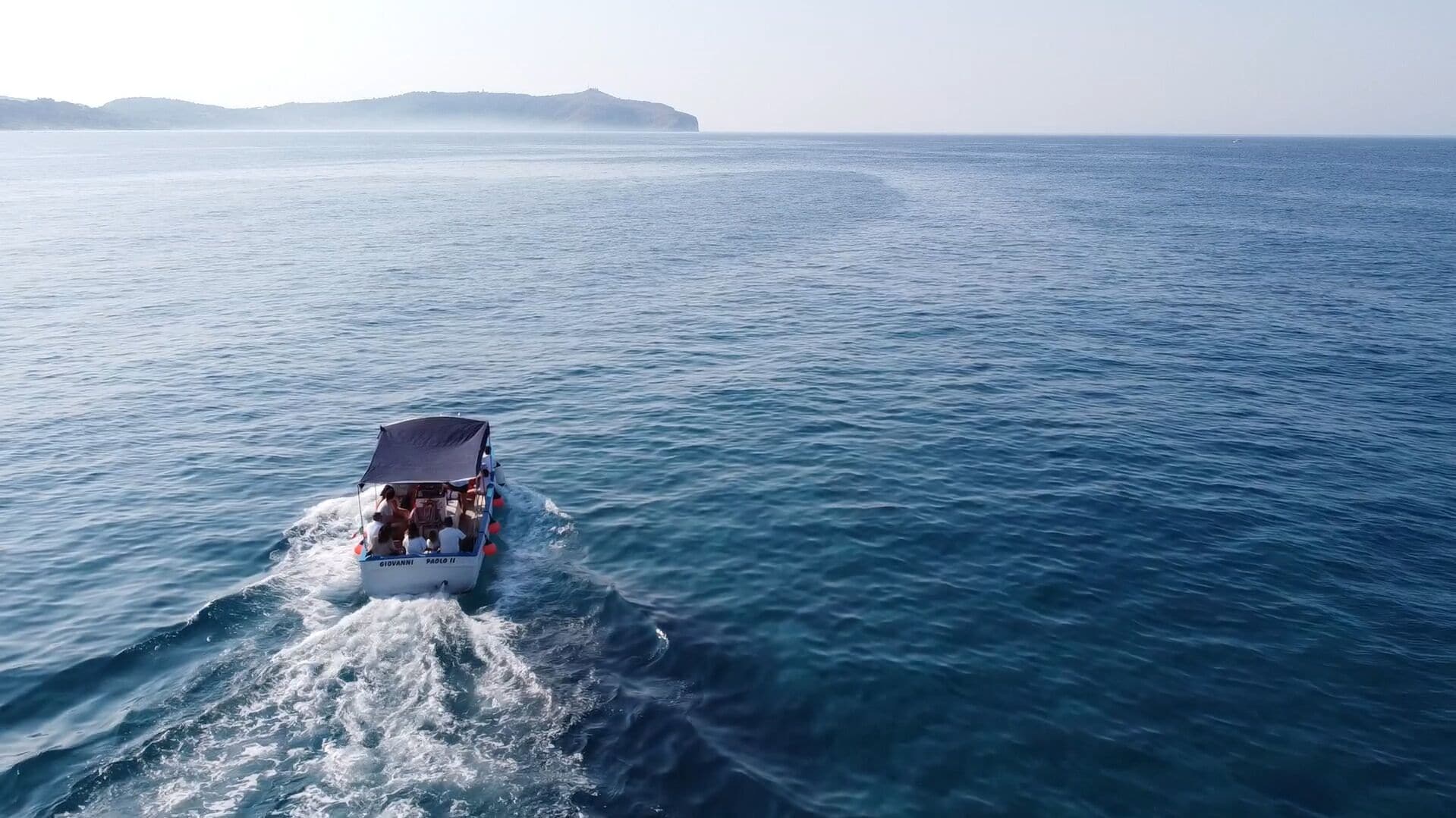 A boat with "GIOVANNI" and "PAOLO II" on its side, moving through a calm sea with a distant landmass.