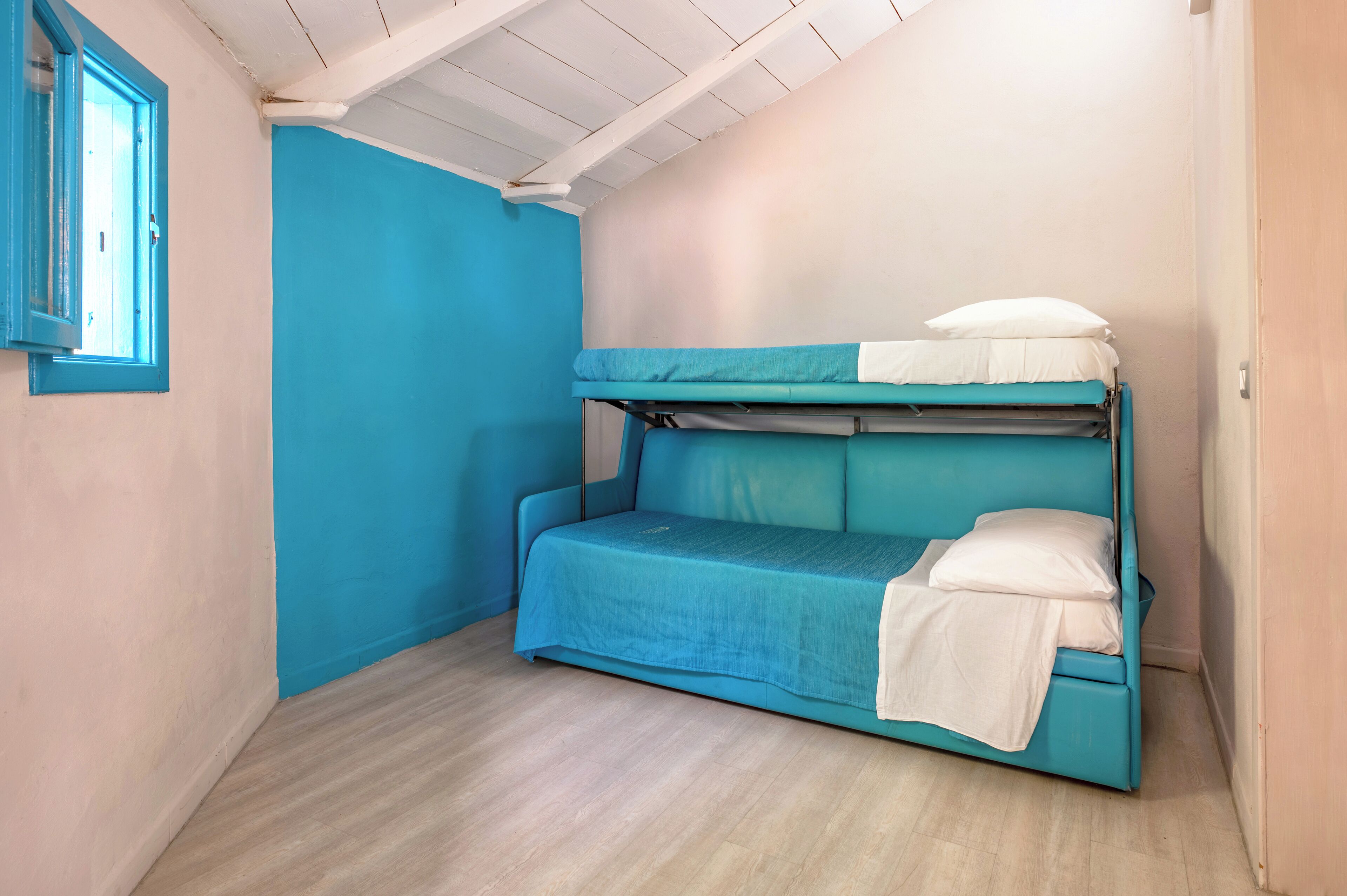Une petite chambre avec un lit simple, un mur bleu et une fenêtre.