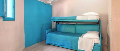 Une petite chambre avec un lit simple, un mur bleu et une fenêtre.