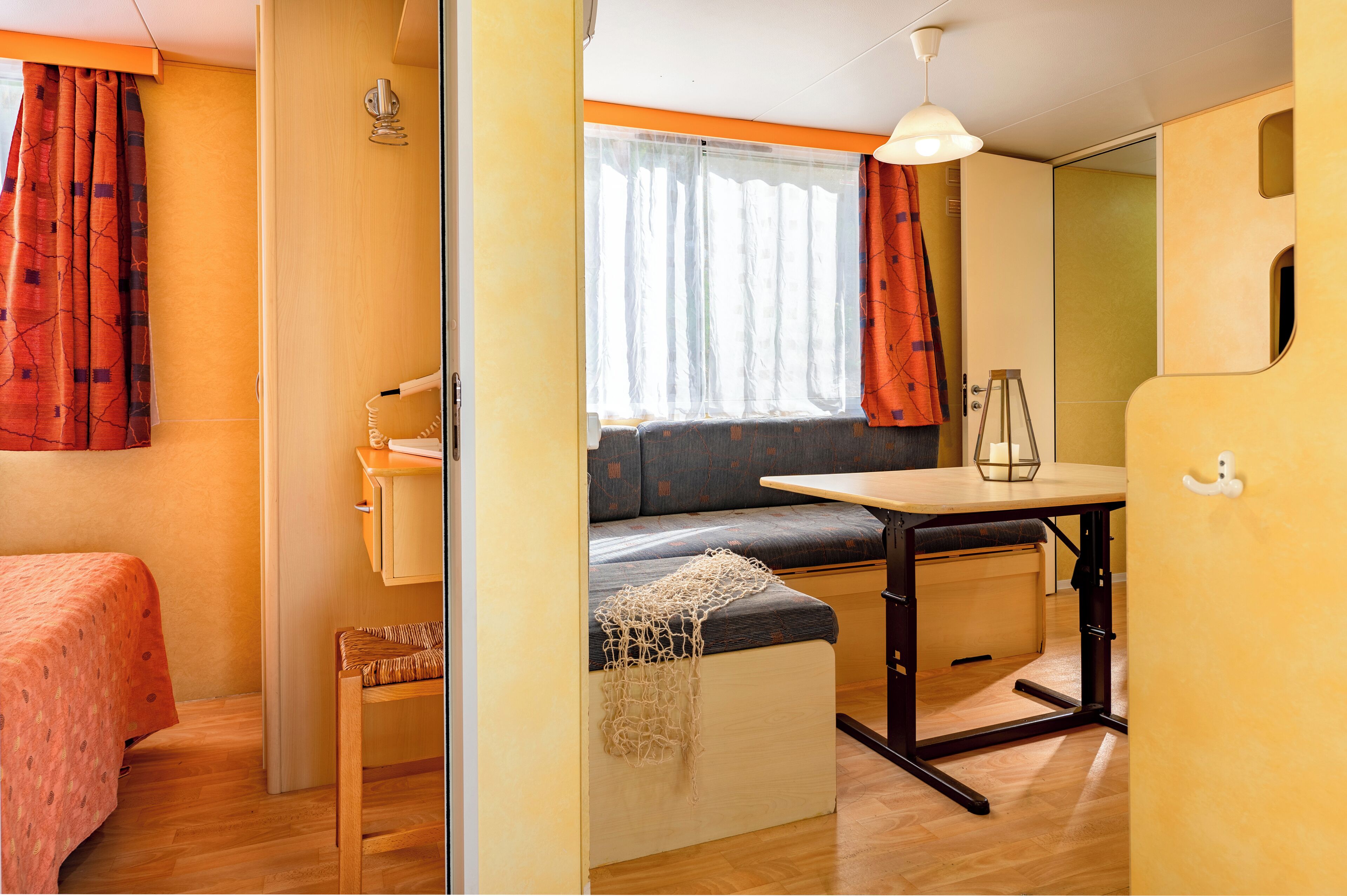A compact room with a bed, a small table, a bench, and a window with curtains.