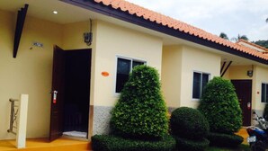A building with a tiled roof, a set of stairs leading to the entrance, and three well-maintained bushes. - At Lamai Resort (Koh Samui)