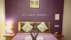 A hotel room with a purple bedspread, two pillows with floral patterns, and a heart-shaped towel arrangement on the bed. - At Lamai Resort (Koh Samui)