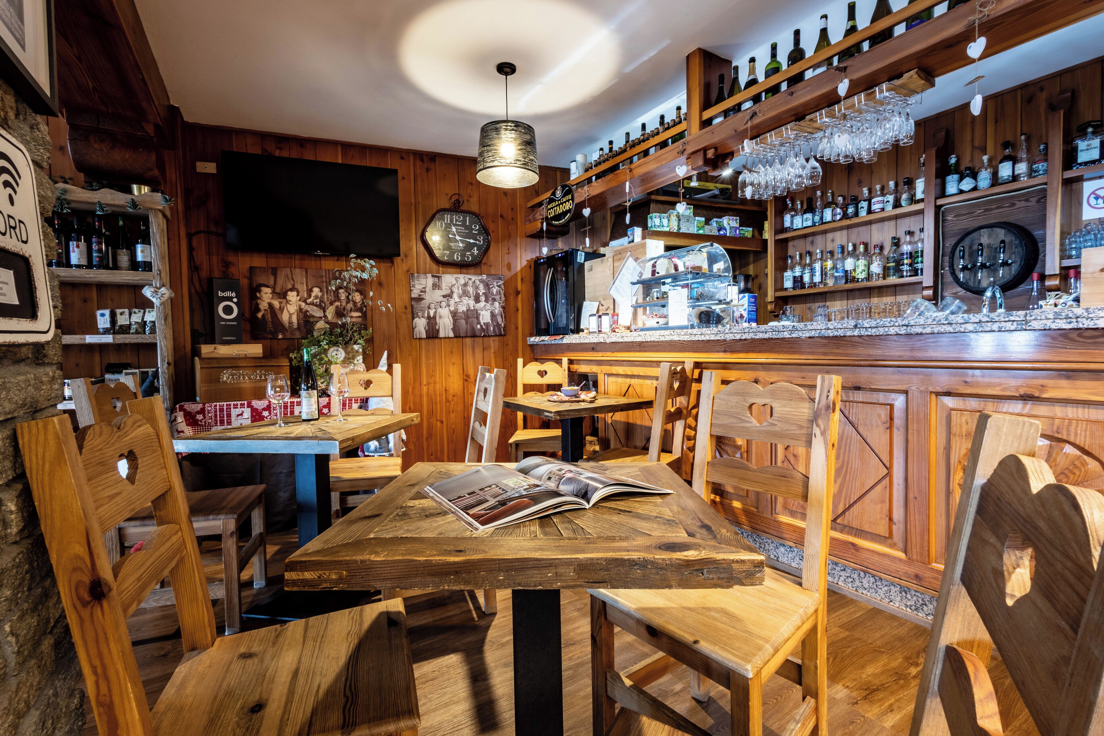 Un rústico área de bar con muebles de madera, estantes llenos de botellas y un televisor colgado en la pared.