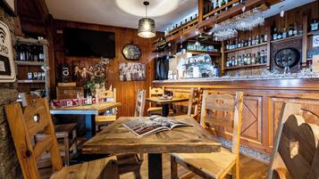 Un rústico área de bar con muebles de madera, estantes llenos de botellas y un televisor colgado en la pared.