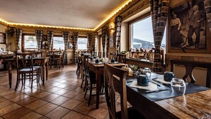 Un restaurante con mesas y sillas de madera, piso de baldosas y un amplio ventanal con cortinas.