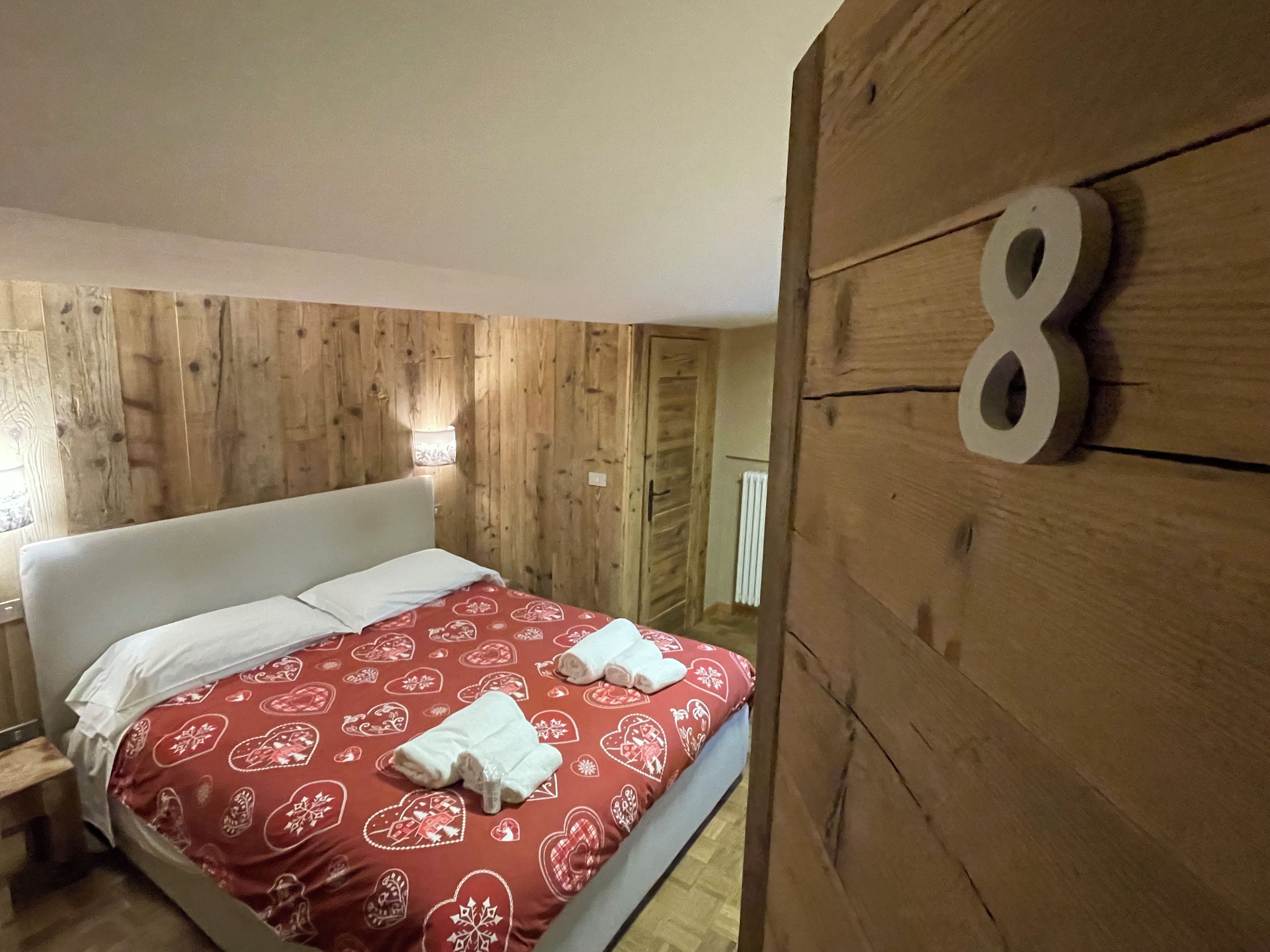 Habitación de hotel con pared de madera, cama con cubrecama rojo estampado y el número 8 en la pared.