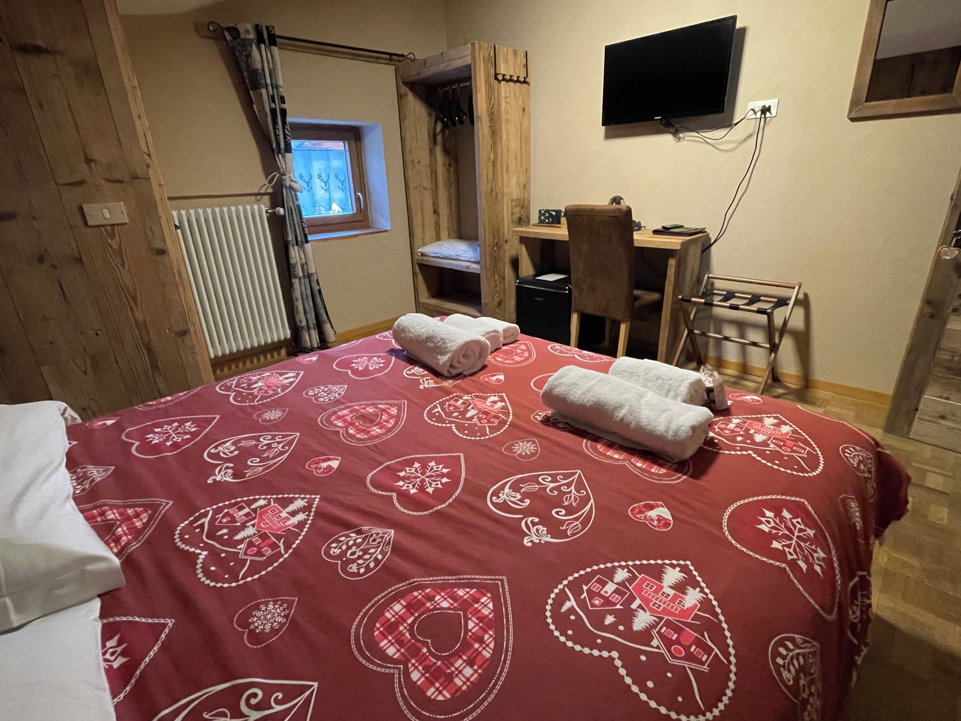 Una habitación con cama, escritorio, silla, televisor y ventana con cortinas.