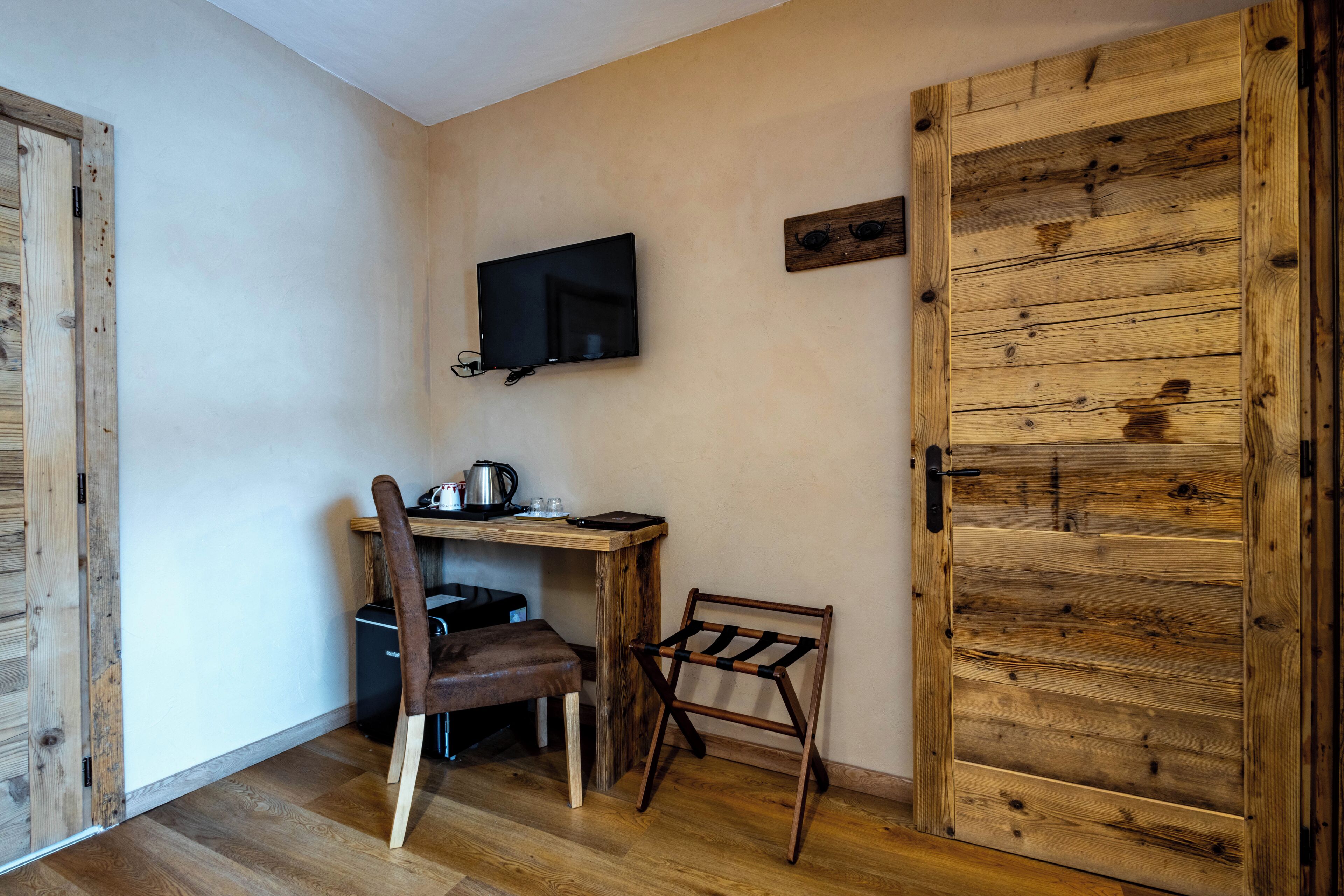Une petite pièce avec un bureau en bois, une chaise et un téléviseur fixé au mur.