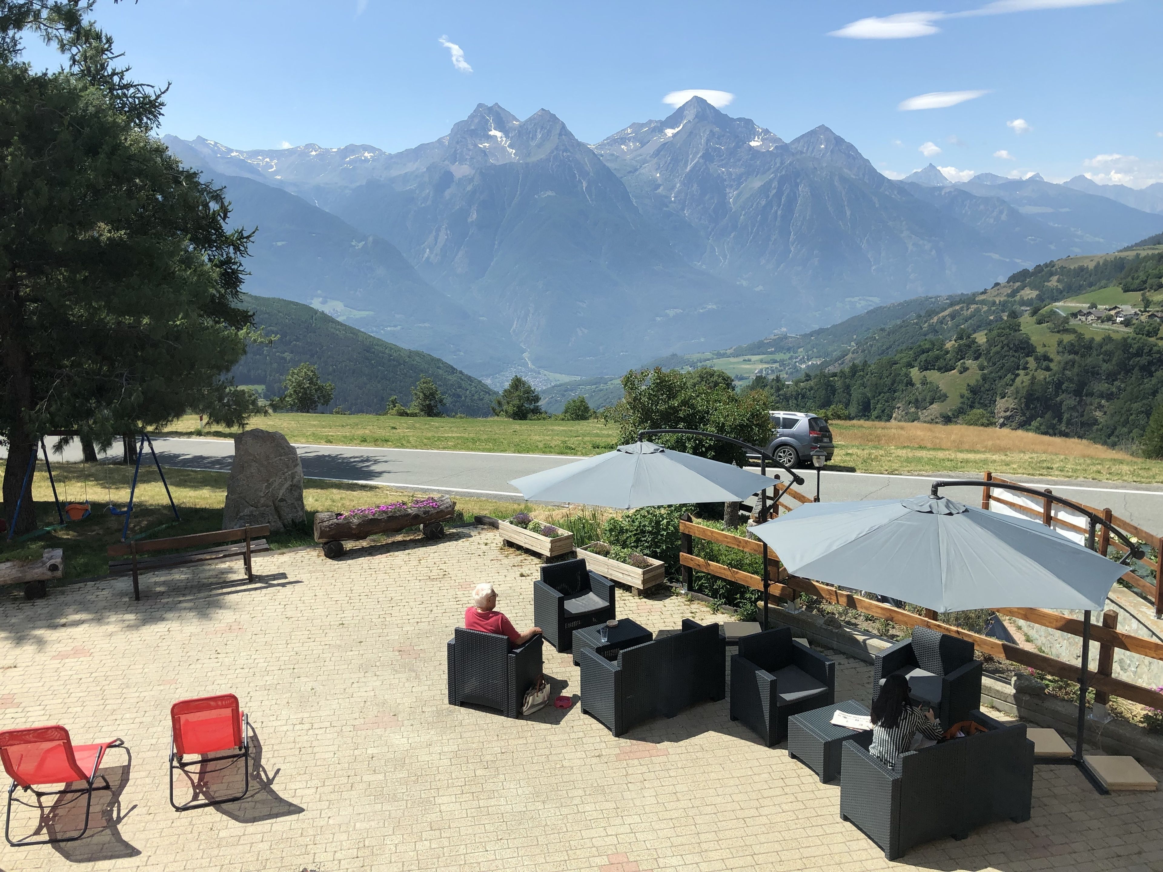 Ein Sitzbereich im Freien mit Korbmöbeln und Sonnenschirmen mit Blick auf eine Straße und Berge.