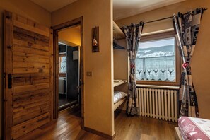 Un dormitorio con un armario de madera, una ventana con cortinas estampadas, un radiador y vistas a un paisaje nevado.
