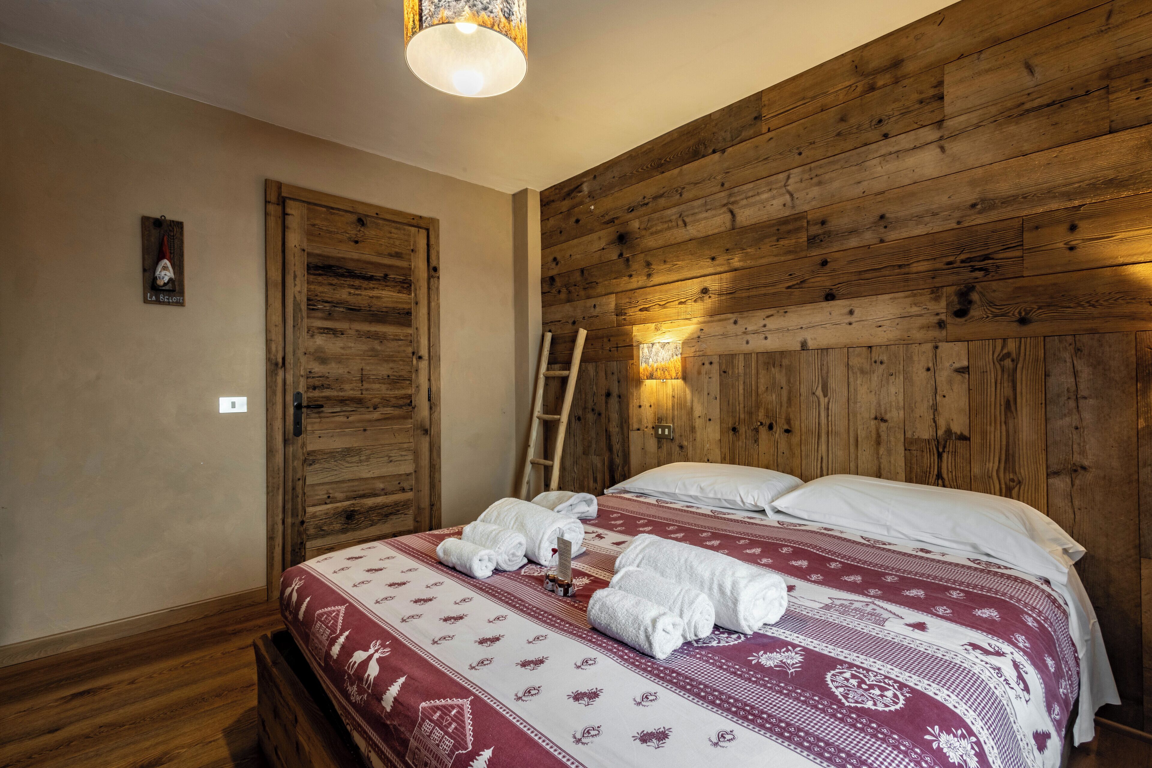 Un dormitorio con paneles de madera, una cama, toallas y una escalera contra la pared.
