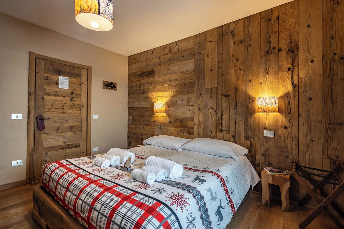 Une pièce aux murs lambrés, avec un lit, deux lampes fixées au mur et un petit tabouret en bois.