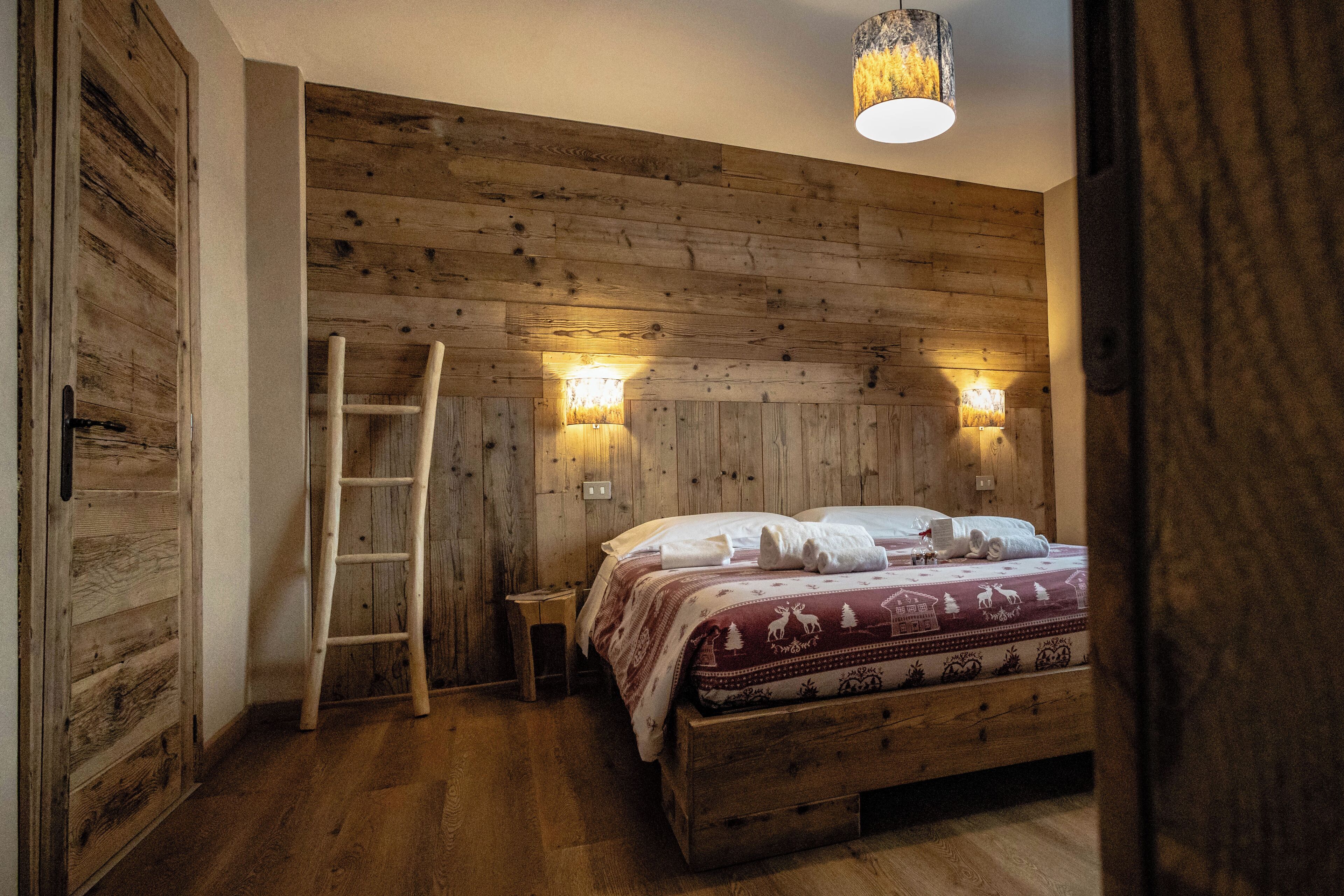 Une pièce aux murs lambrés, avec un lit, une échelle et des lampes fixées au mur.