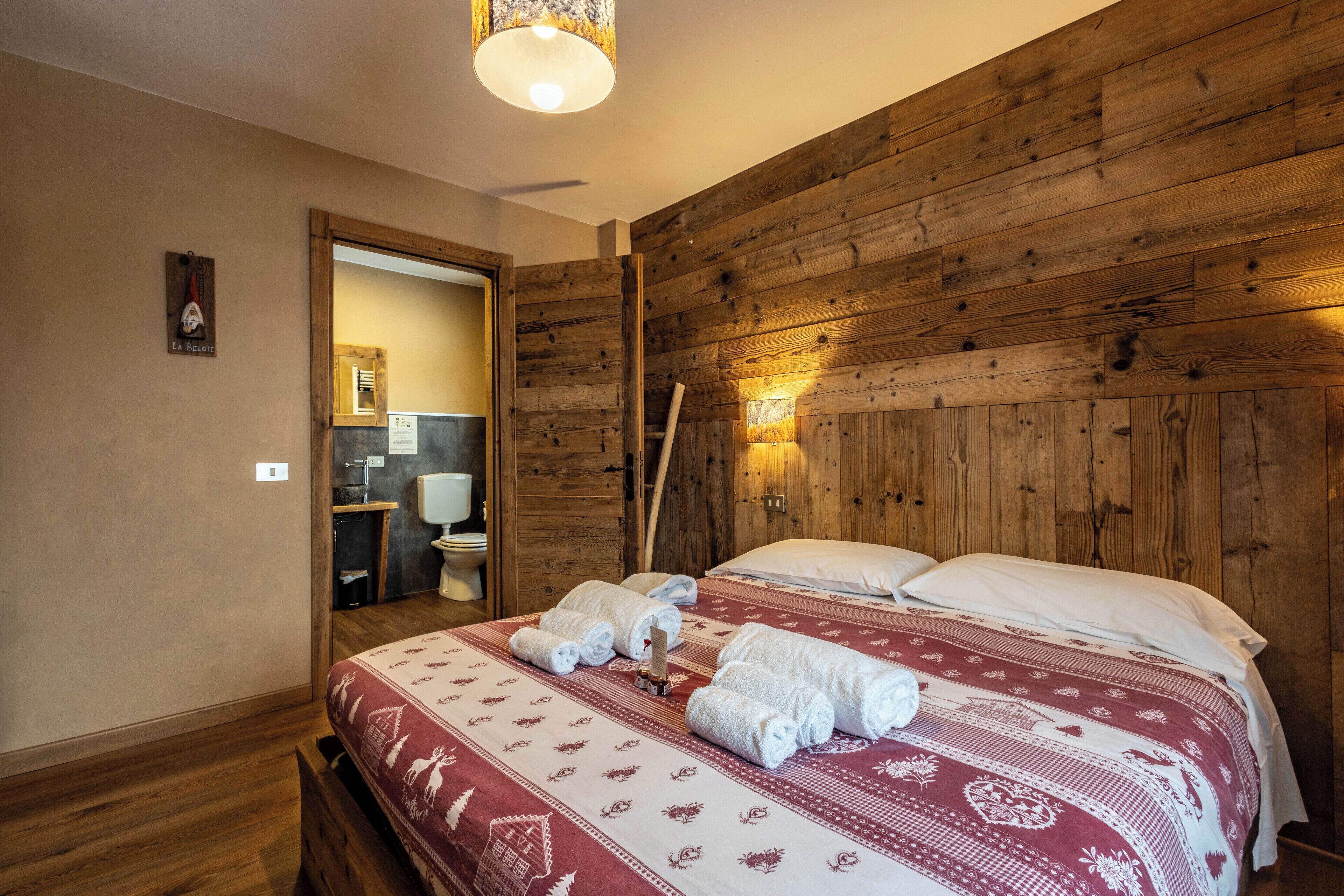 A wooden-paneled room with a bed, towels, and a wooden door leading to a bathroom.