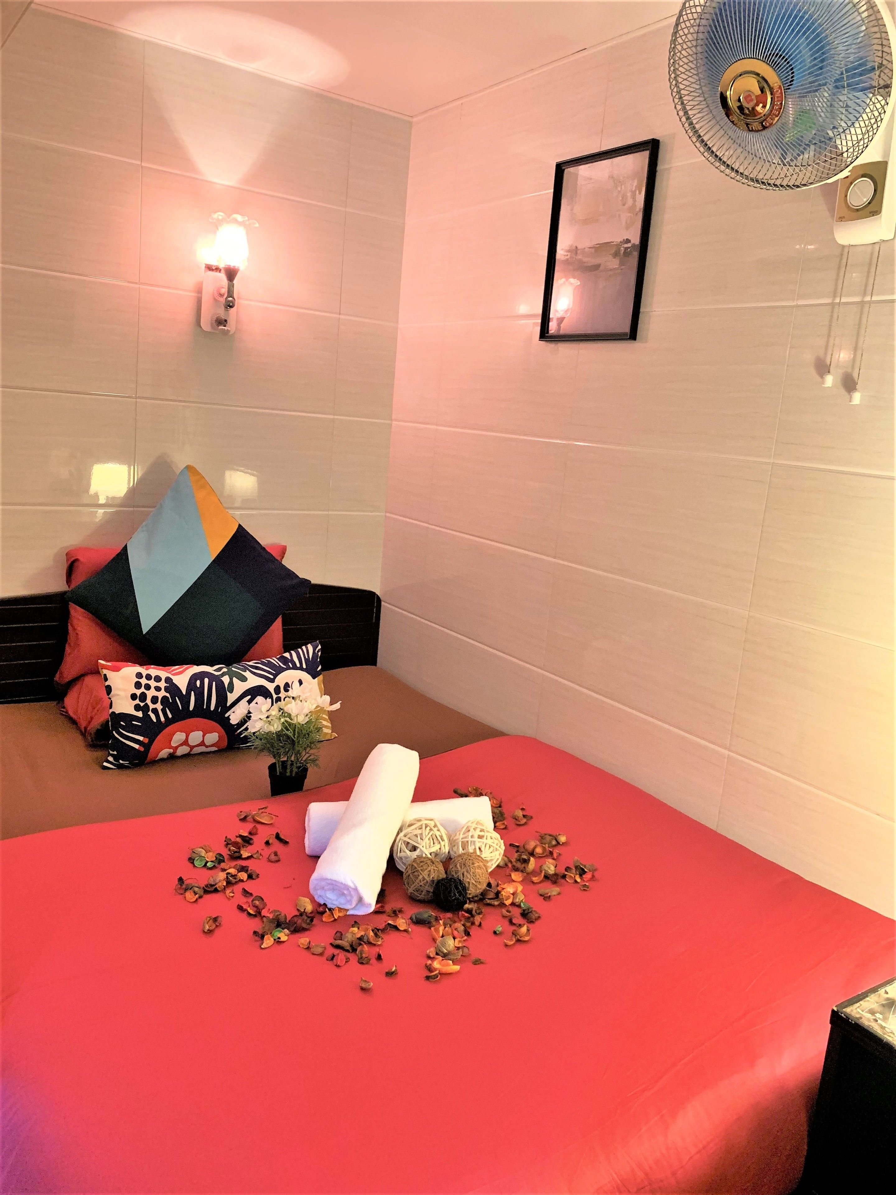 A hotel room with a bed, pillows, a wall-mounted light, a fan, and a framed picture.