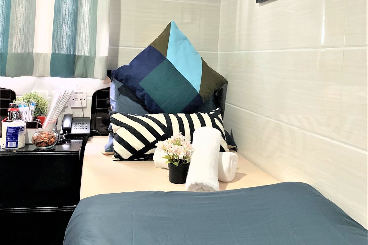 A hotel room with a bed, a bedside table with a phone, a small plant, and a painting on the wall.