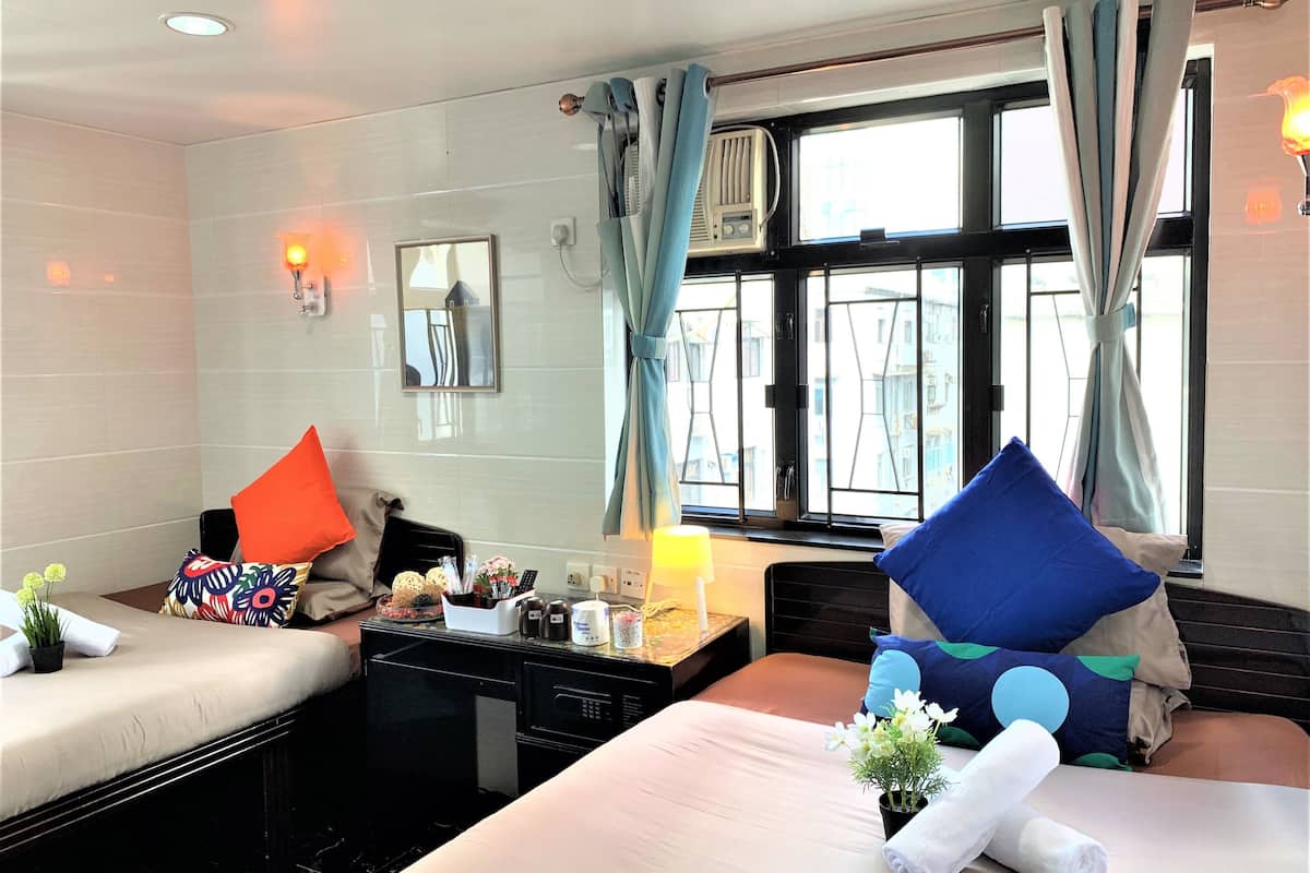A hotel room with two beds, a small table with a lamp, a mirror, and a window with curtains.