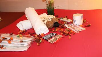 A neatly arranged table with towels, toiletries, and decorative items on a red tablecloth.
