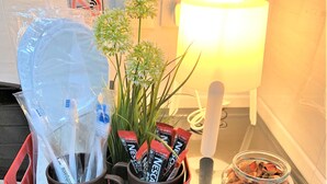 Habitación de hotel con una mesita de noche que sostiene artículos de aseo, una lámpara y un tarro de vidrio con flores secas.