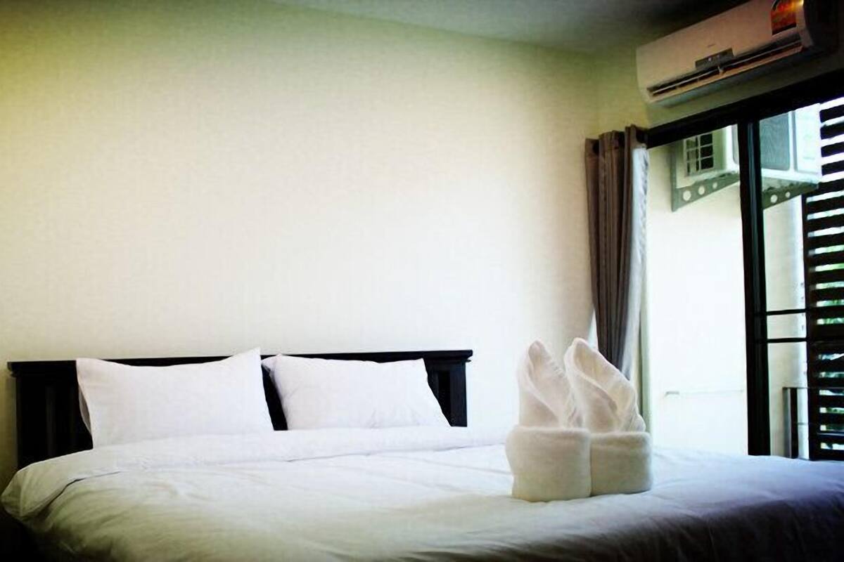 A hotel room with a bed, a nightstand, a lamp, and a window with blinds.