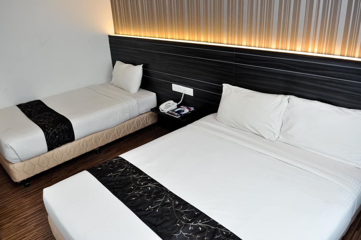 Quarto de hotel com uma cama grande, duas camas menores, telefone de apoio e luminária fixada na parede.