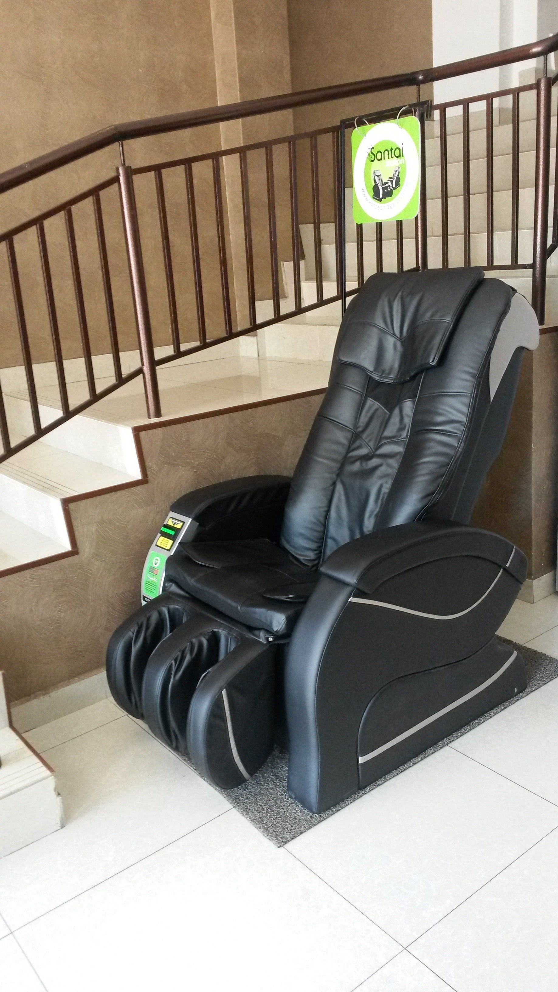 A massage chair in a room with a staircase and a sign above it.