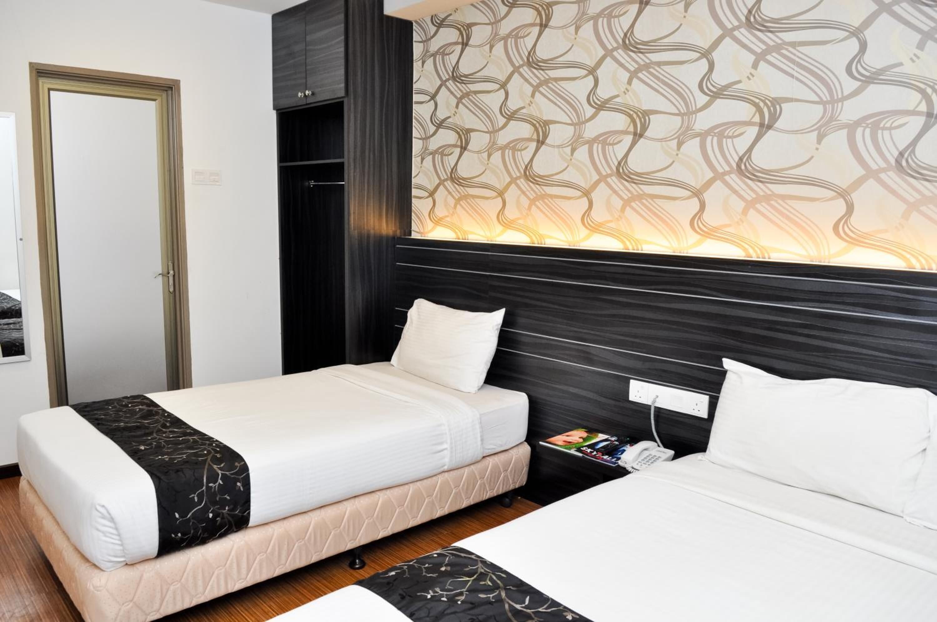Une chambre d’hôtel avec deux lits, une armoire, un mur décoré de motifs et une table de chevet avec un téléphone.