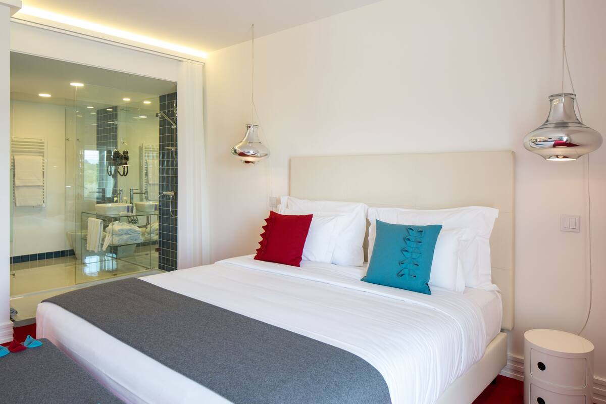 A modern hotel room with a large bed, a glass shower area, and a white color scheme.
