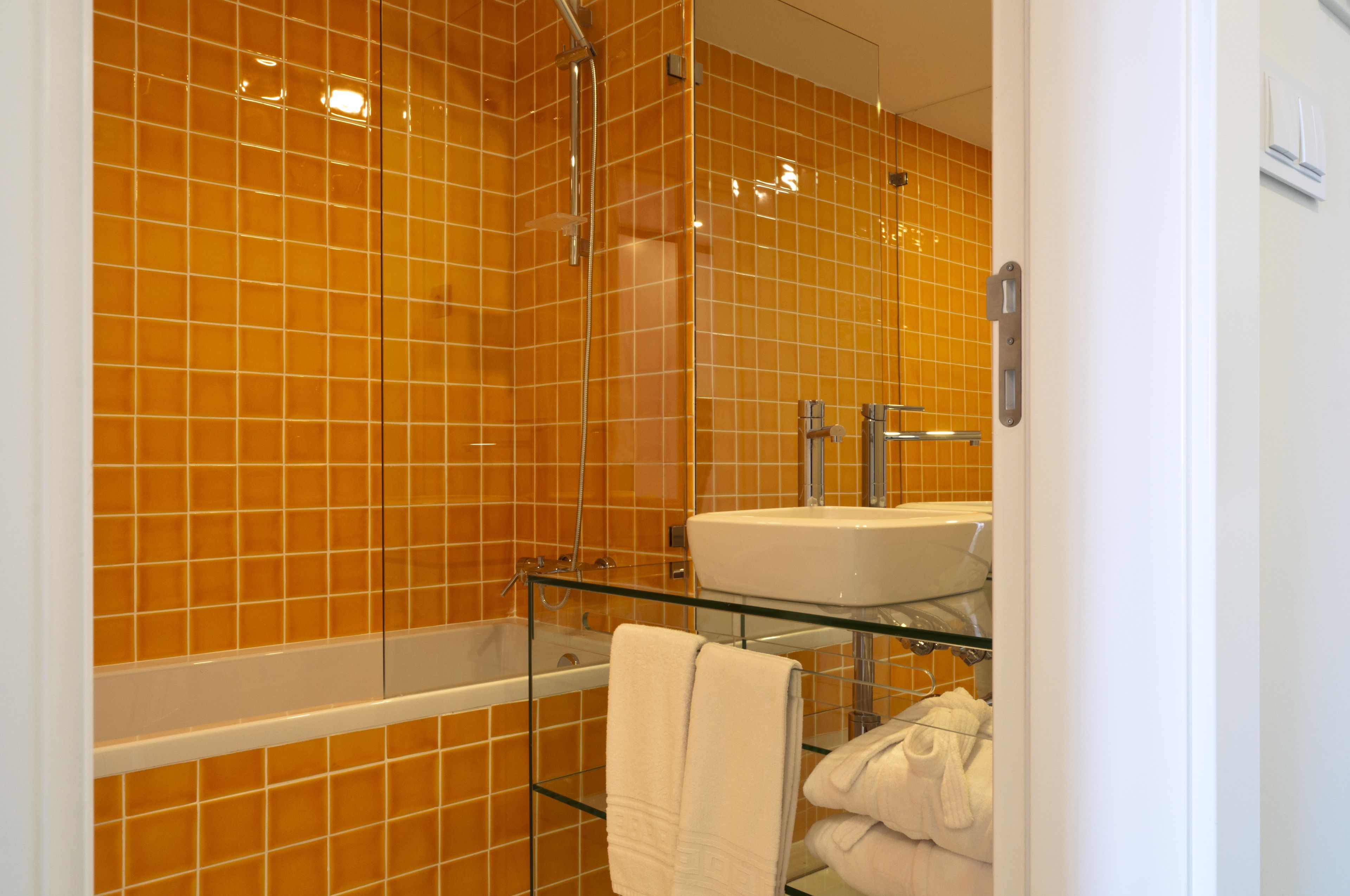 A bathroom with orange tiles, a glass shelf with towels, and a white sink.
