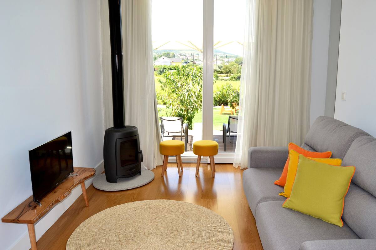A living room with a flat-screen TV, a fireplace, a sofa with cushions, and a view of the outdoors.