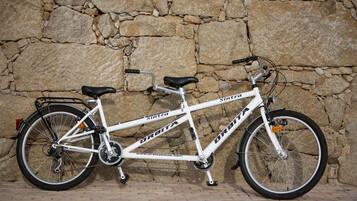 Una bicicleta blanca con los nombres de marca 'Sintra' y 'Orbitia' a la vista, apoyada contra una pared de piedra.