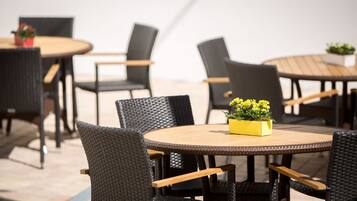 An outdoor seating area with round tables and wicker chairs.