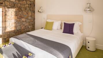 Un dormitorio con pared de piedra, una cama con edredón gris y blanco, y dos lámparas de noche.