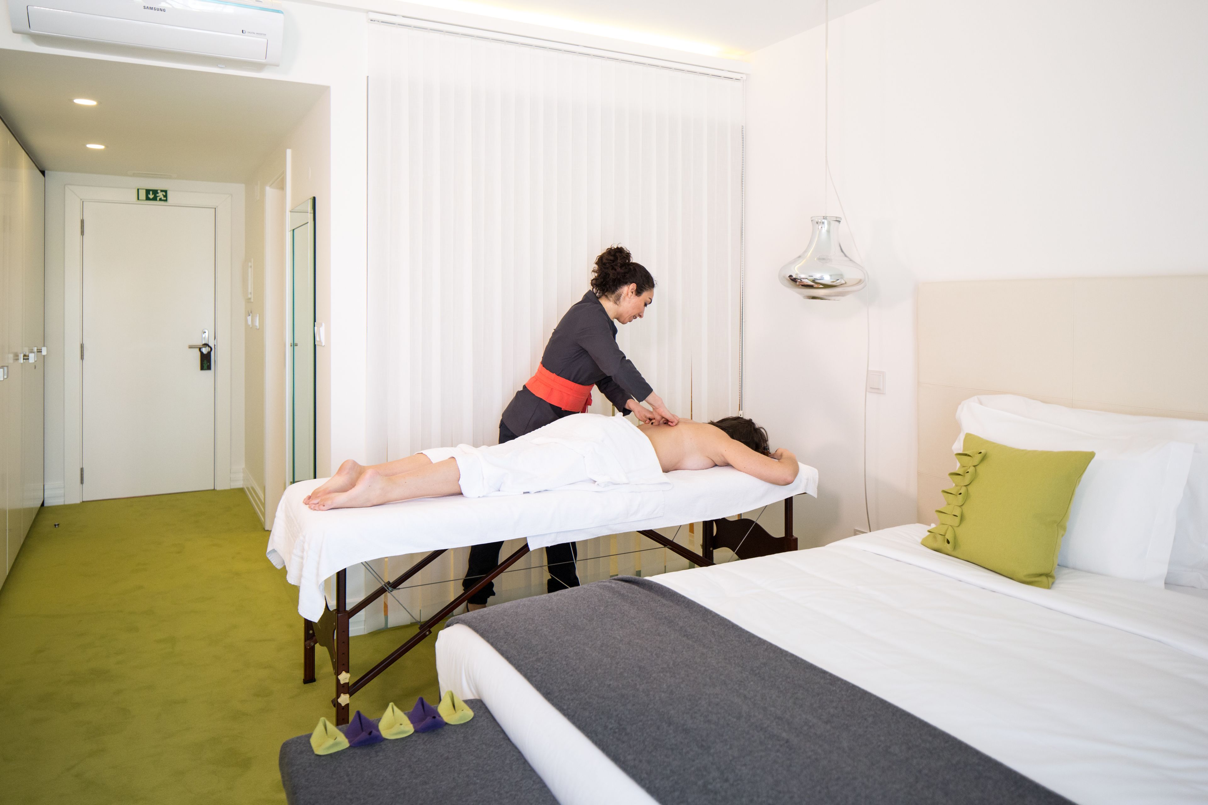 A massage therapy room with a bed, a massage table, and a massage therapist attending to a client.
