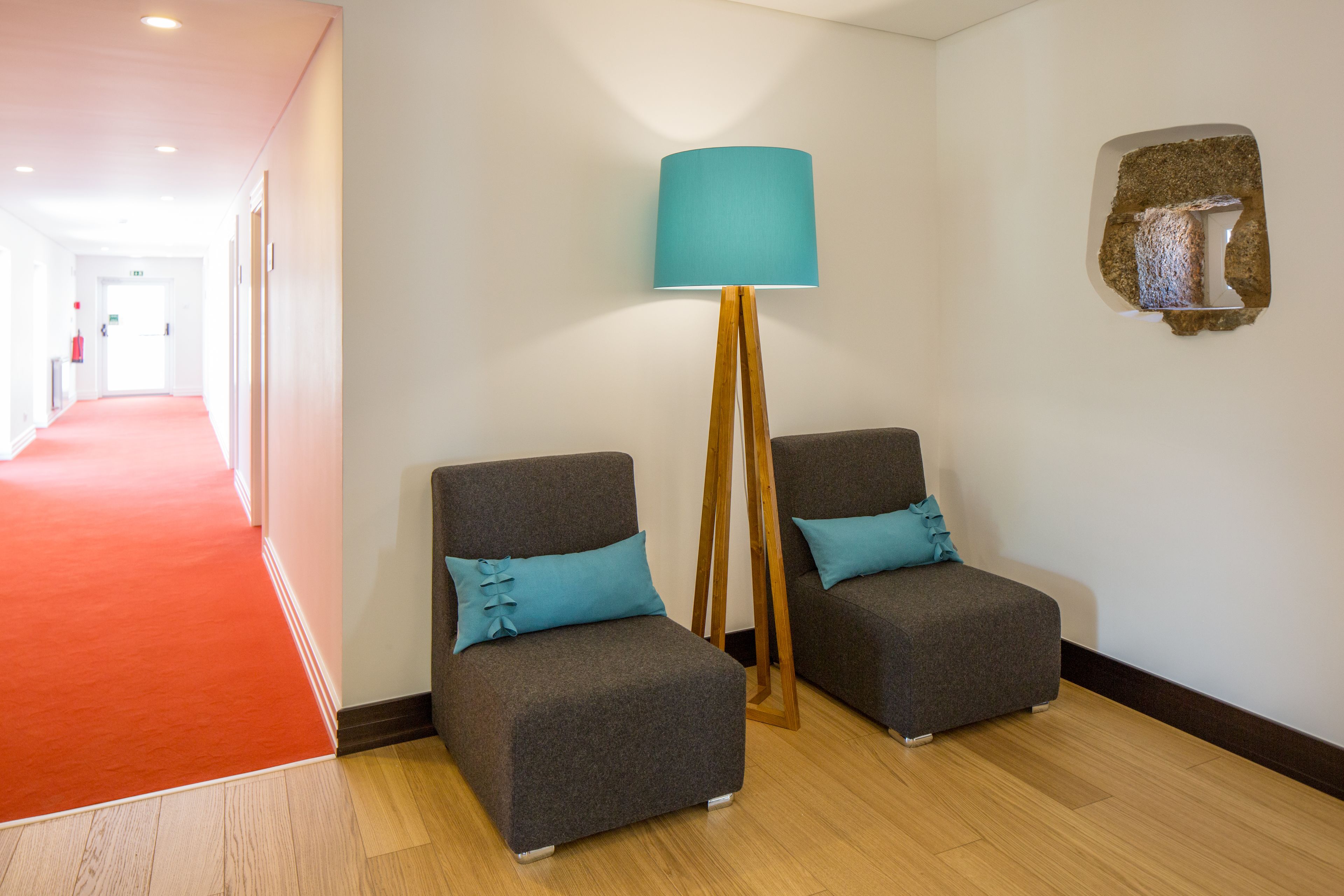 Un pasillo con alfombra roja que conduce a una habitación con dos sillones grises y una lámpara de pie.